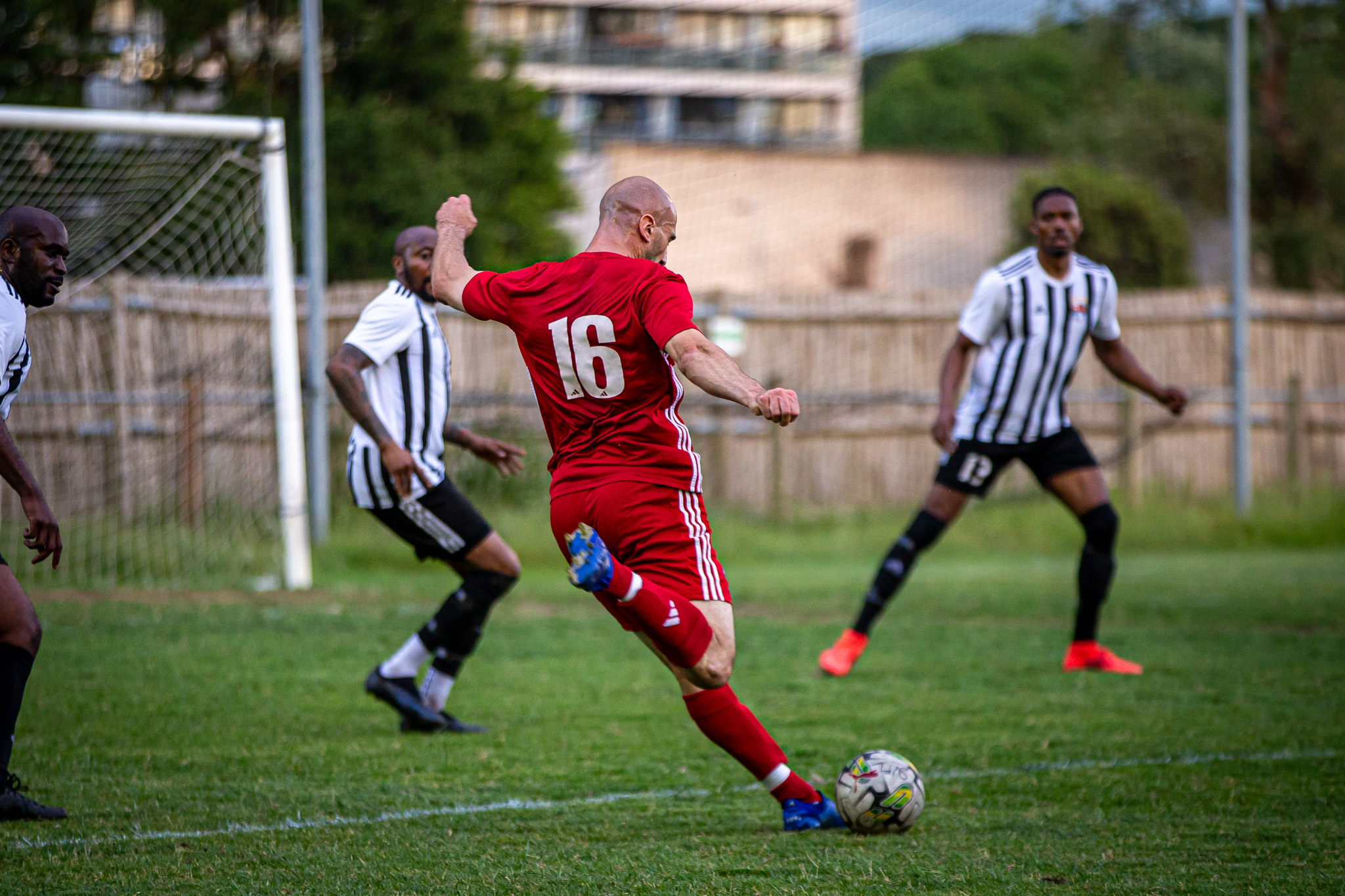 AFC Greenwich Borough men’s vets player in red kit taking a shot on grass pitch, representing football activities linked with GB10.