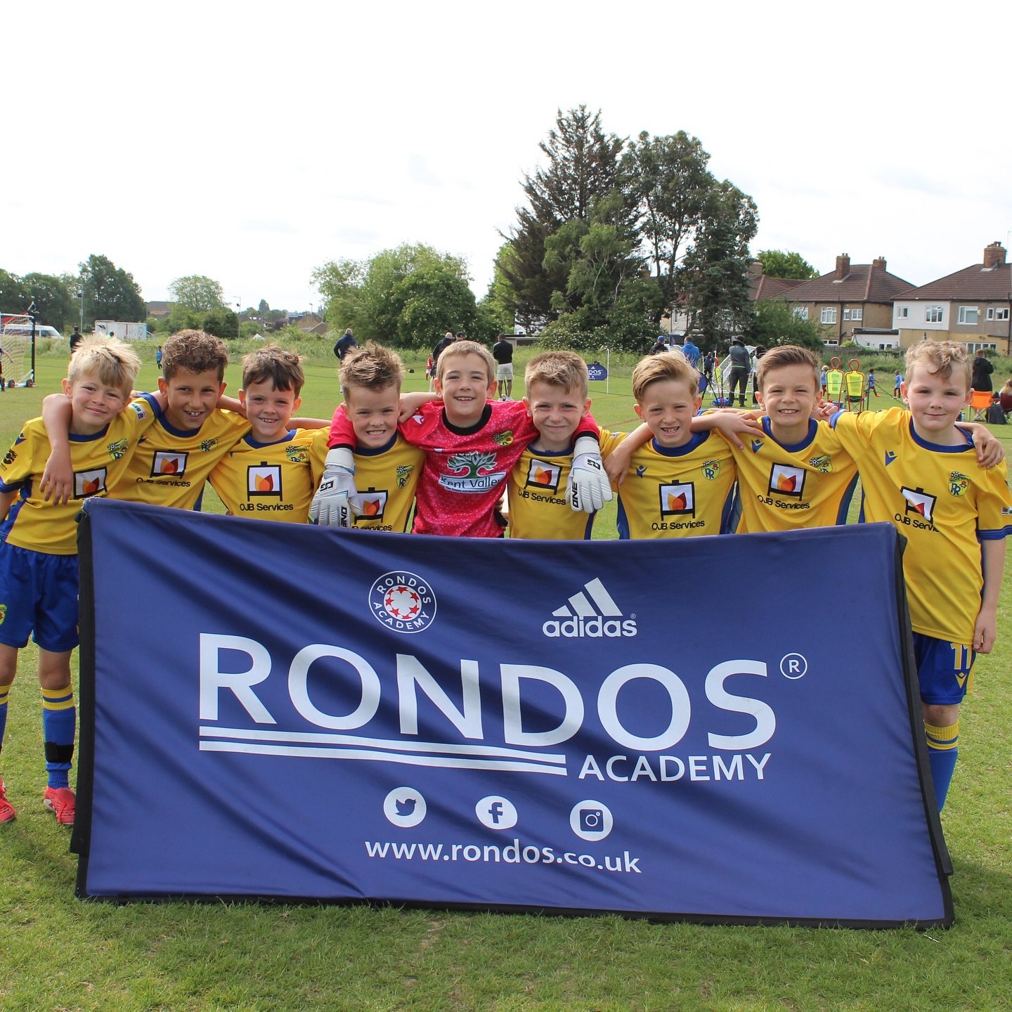 Young football team at a Rondos Academy tournament held at GB10, standing together behind a branded banner on the pitch
