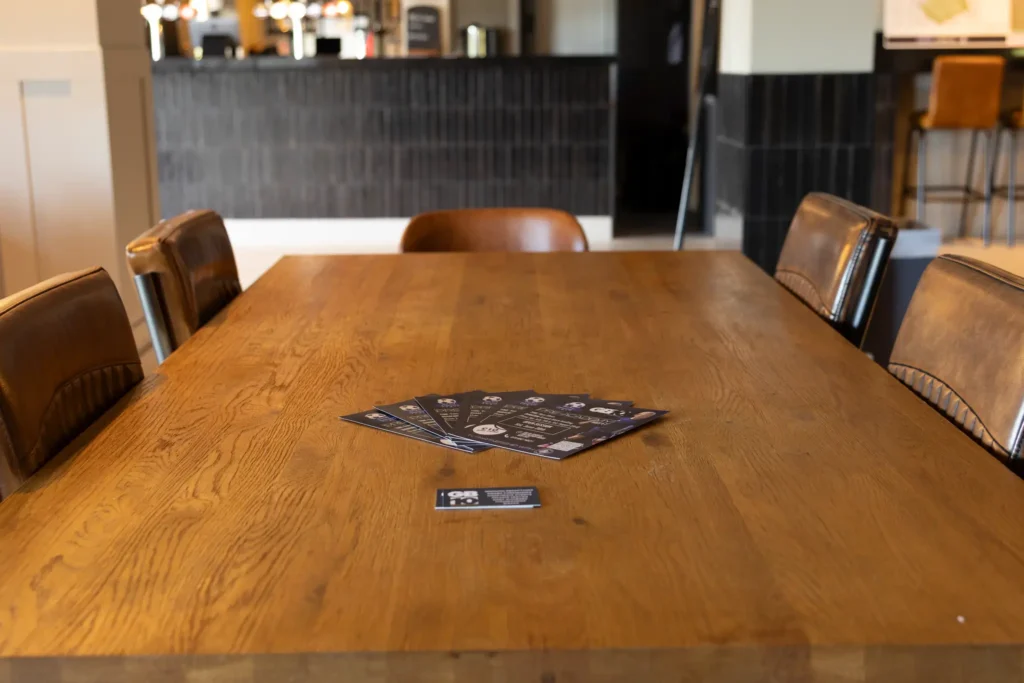 Flyers neatly arranged on a wooden table with leather chairs inside GB10 Sports Hub lounge.
