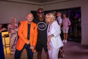Three guests smiling together at GB10 Sports Hub party under purple lighting.