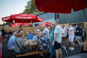 Guests at tables and standing under parasols at GB10 Sports Hub outdoor terrace party.