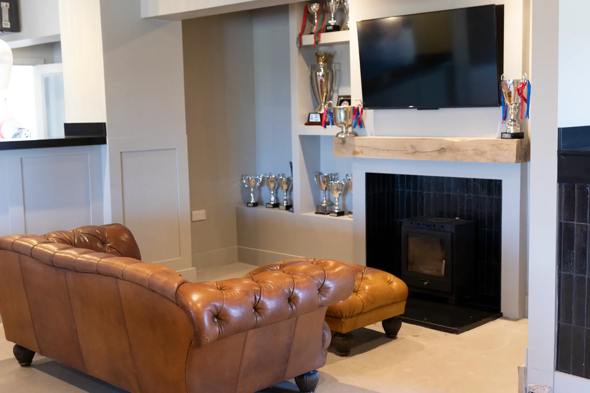 Leather sofa facing trophy shelves and TV screen inside GB10 Sports Hub lounge.