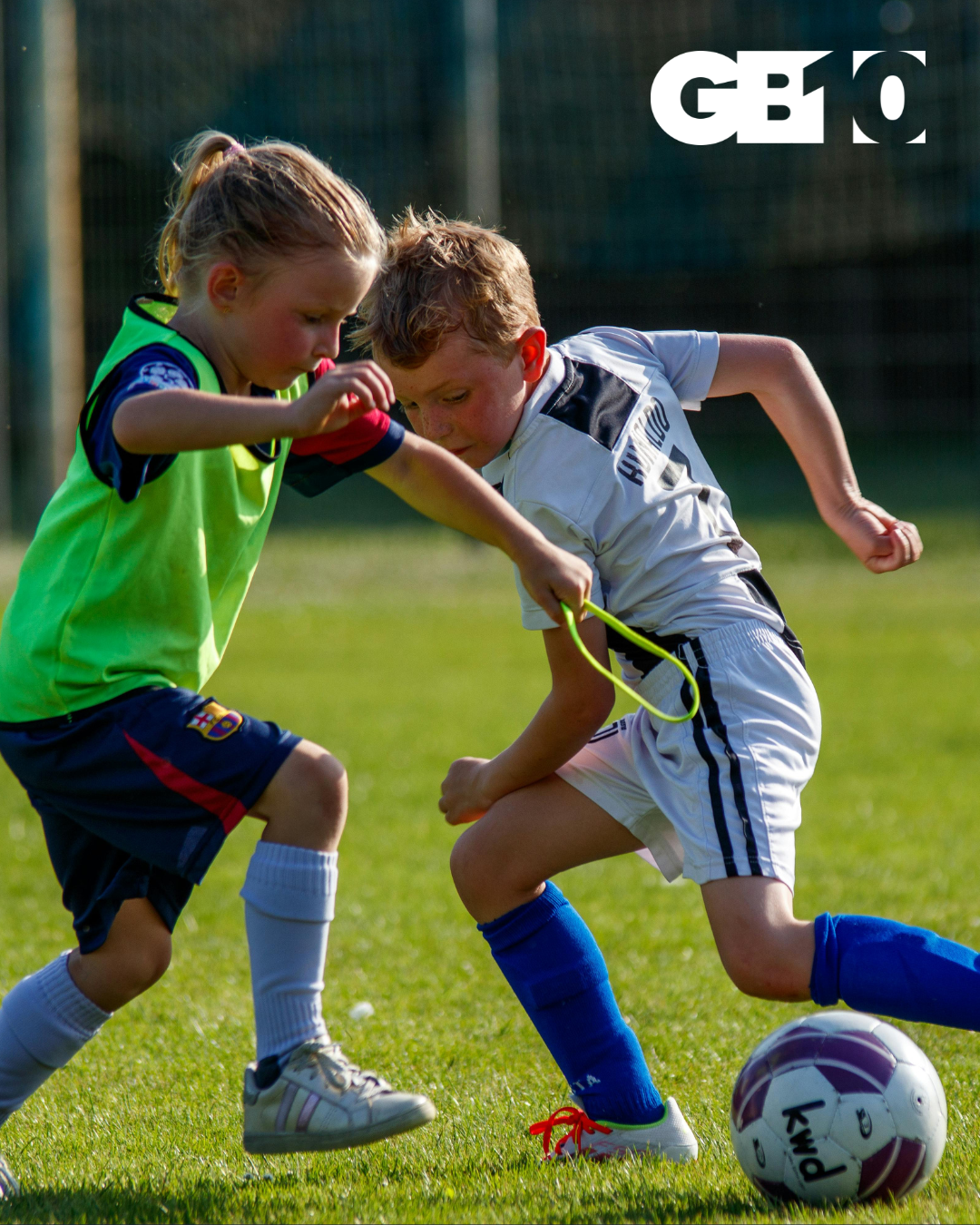 Two young footballers competing for possession on a grass football pitch